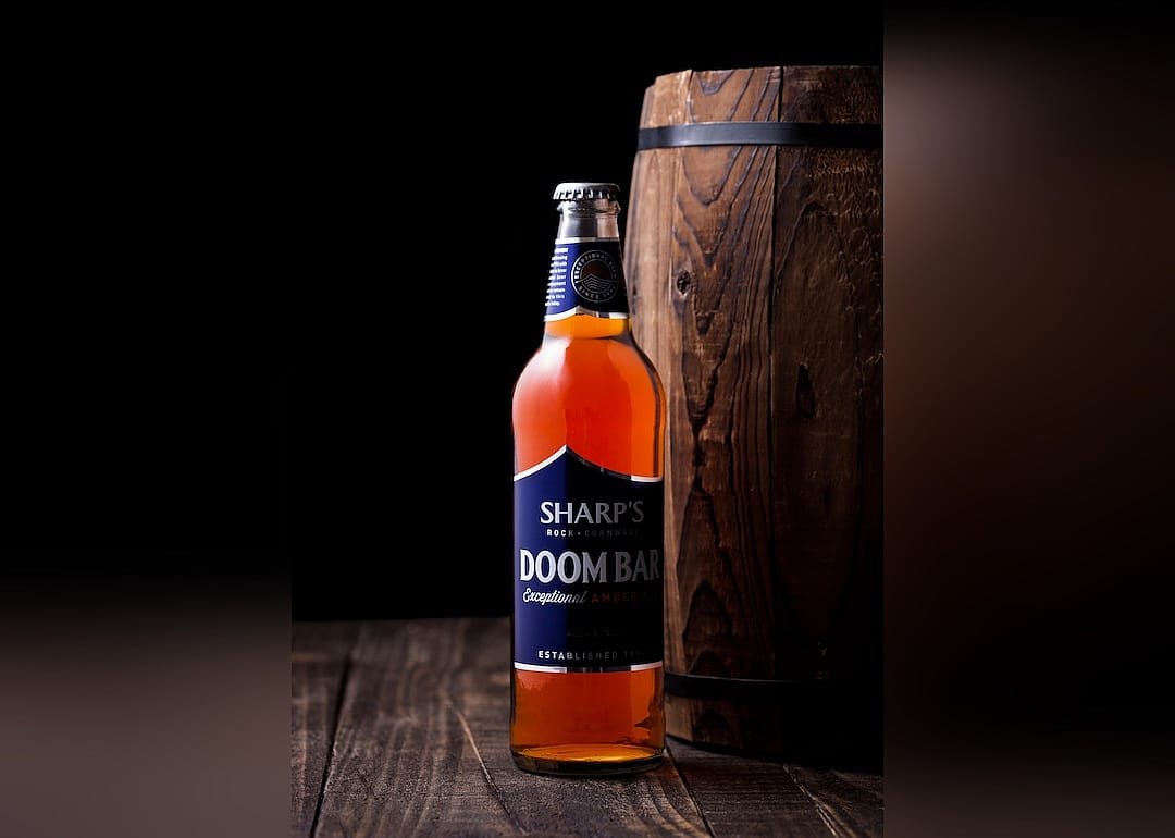 Bottle of Sharp's Doom Bar amber ale on with wooden barrel on a dark background.