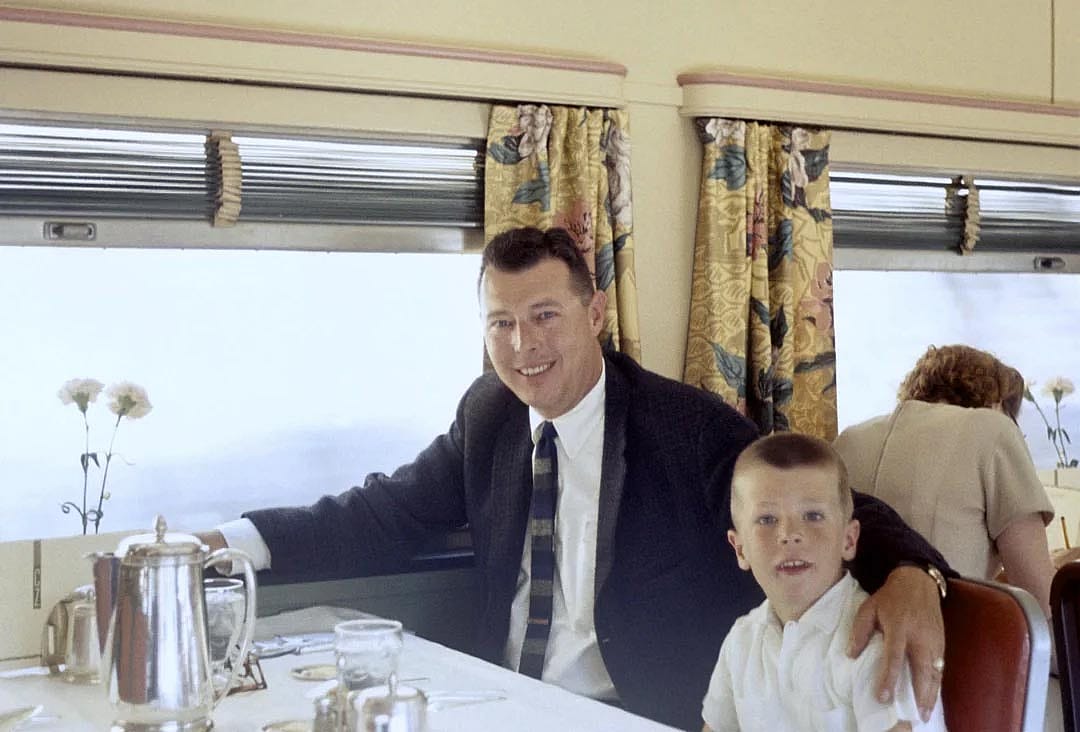 Color photo of a father and son riding on a train.