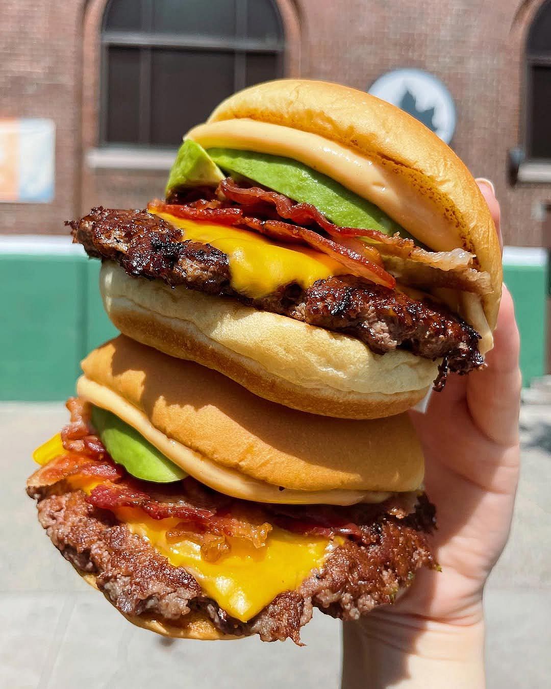 A hand holding two Triple Avocado Bacon Burger from Shake Shack