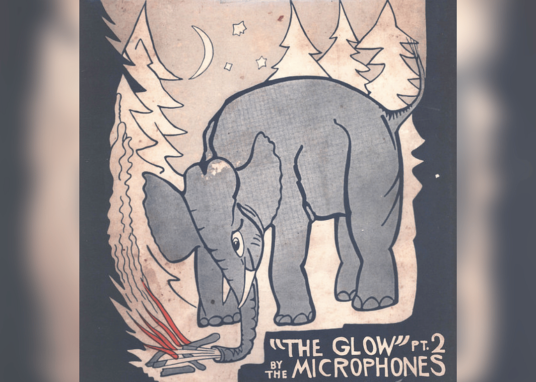 A drawing of an elephant blowing on a campfire with trees in the background.