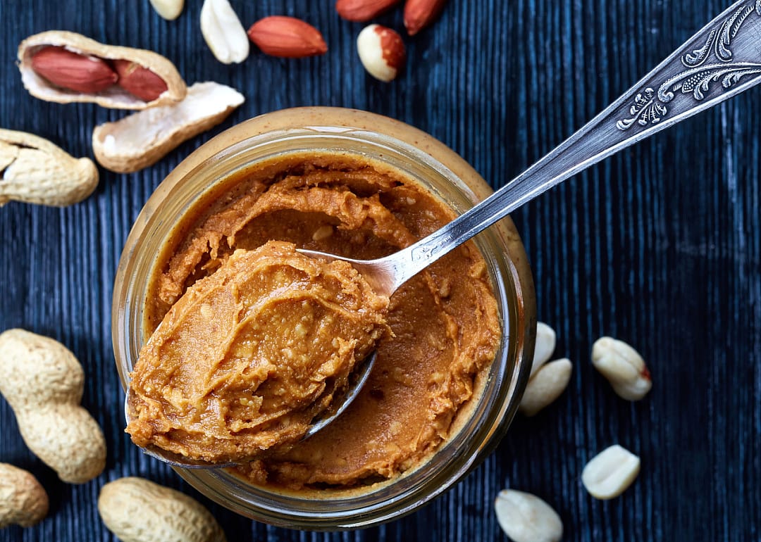 Jar and spoon of peanut butter and peanuts.