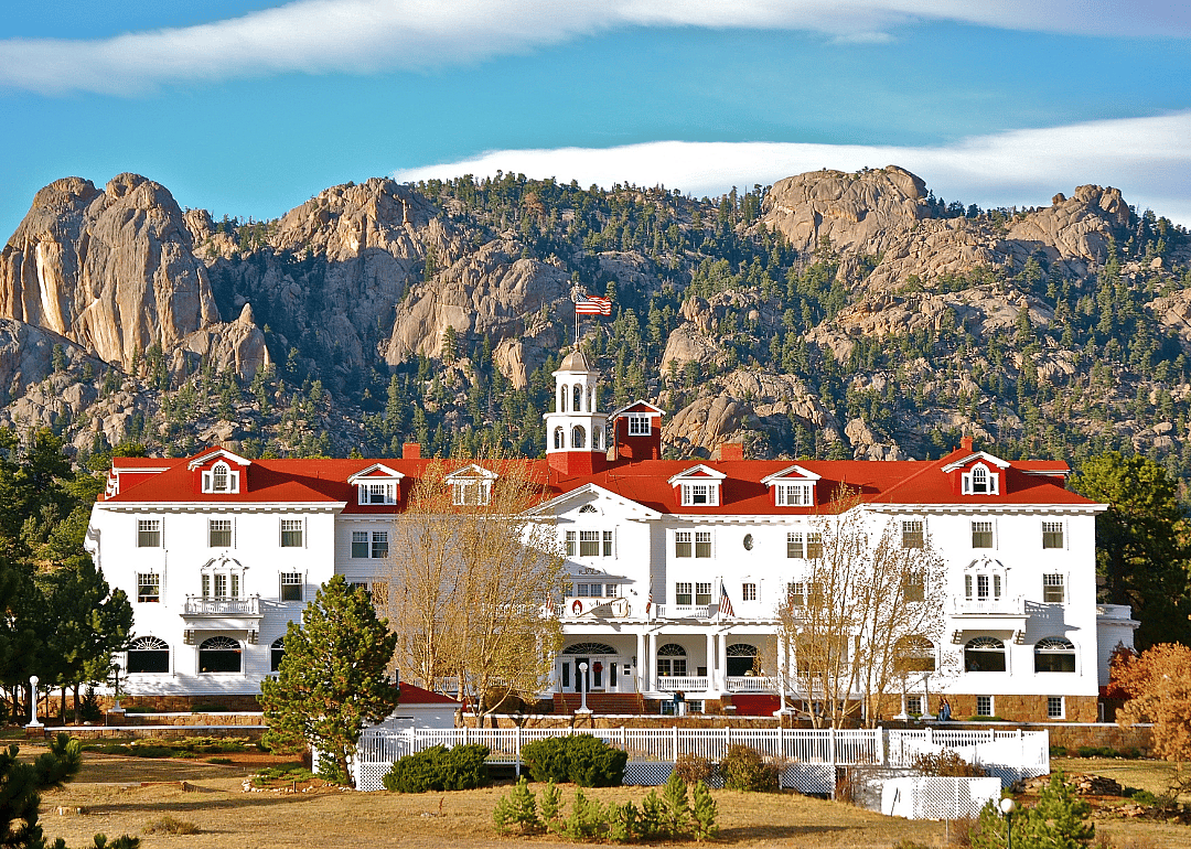 The Stanley Hotel, a large white building with red roof with rocky mountains in the background.