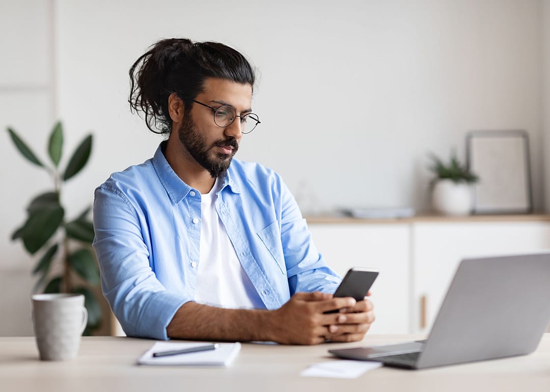 Person with glasses looking at phone and laptop.