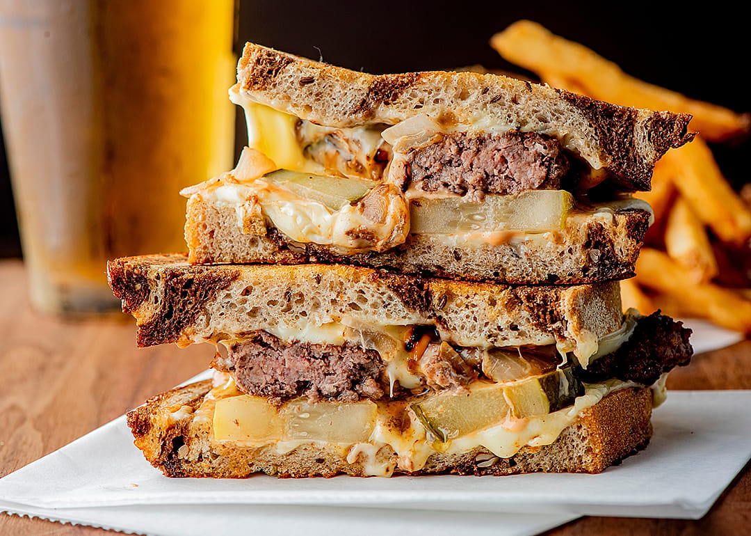 Ground beef patty with melted cheese and topped with caramelized onions on two slices of griddled rye bread.