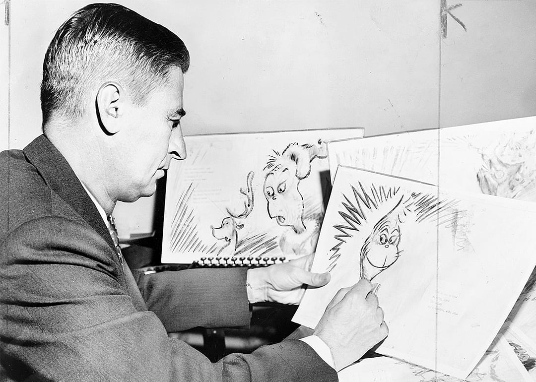 Dr. Seuss Geisel holding illustrations for his book, How the Grinch Stole Christmas.