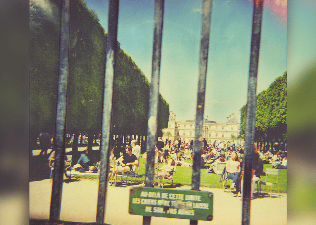 People sitting inside a fenced-in Jardin du Luxembourg in Paris.