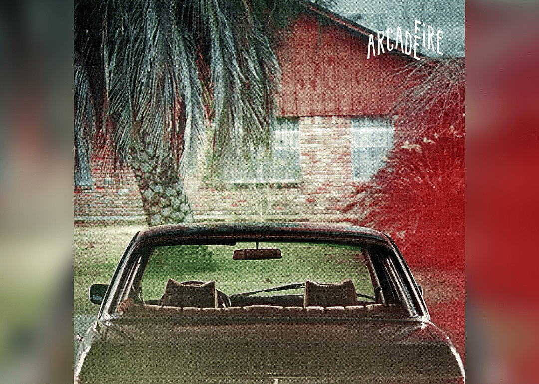 A classic car parked behind a palm tree at a home.