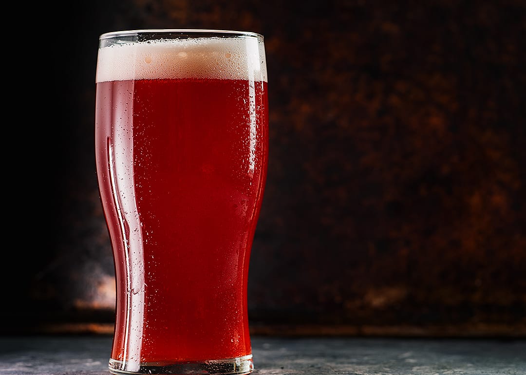 Glass with a red ale on a table mat.
