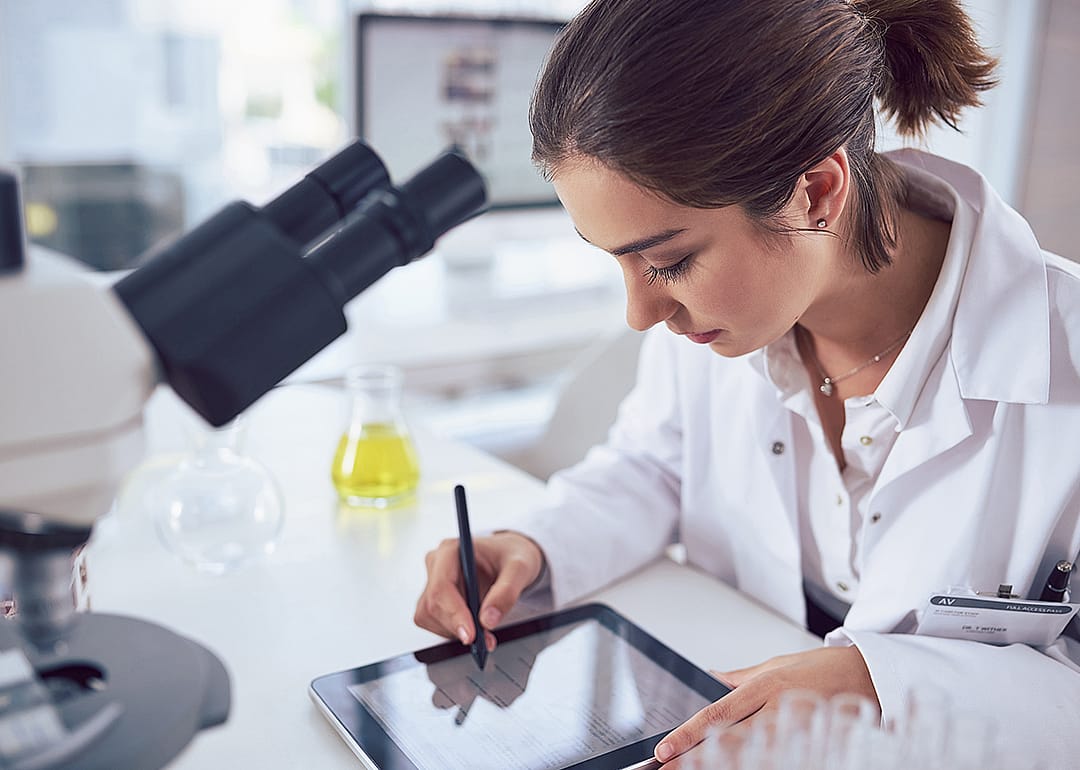 Student working at microscope in lab with tablet.