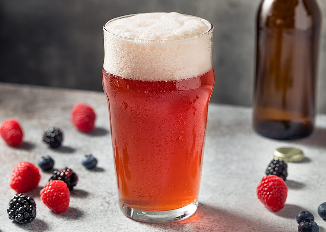 Fruit beer in a glass with berries on table.