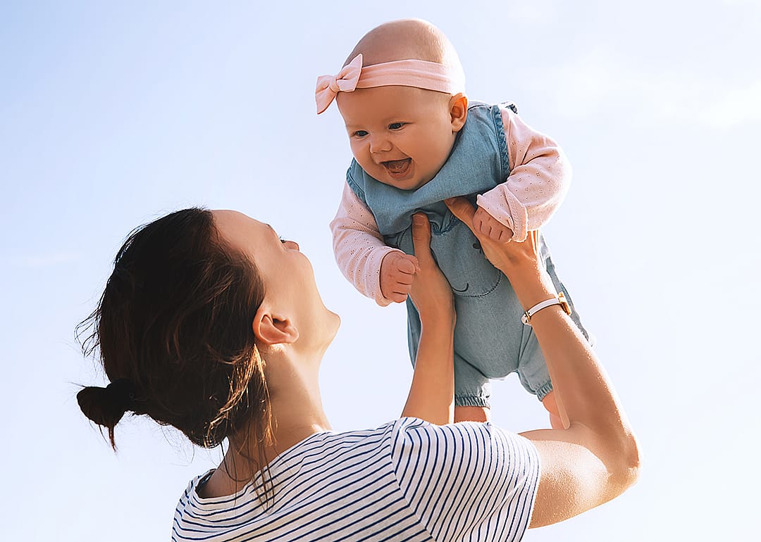 Mother holding baby up outside.