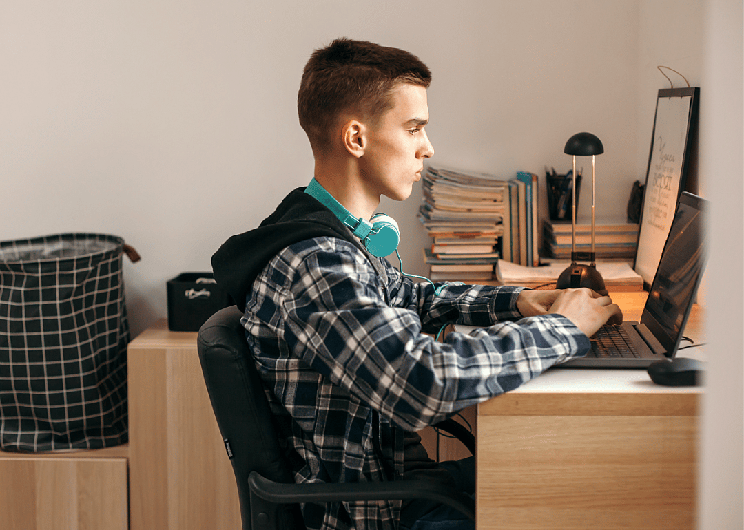 A teen sits at a desk staring intently at a screen.