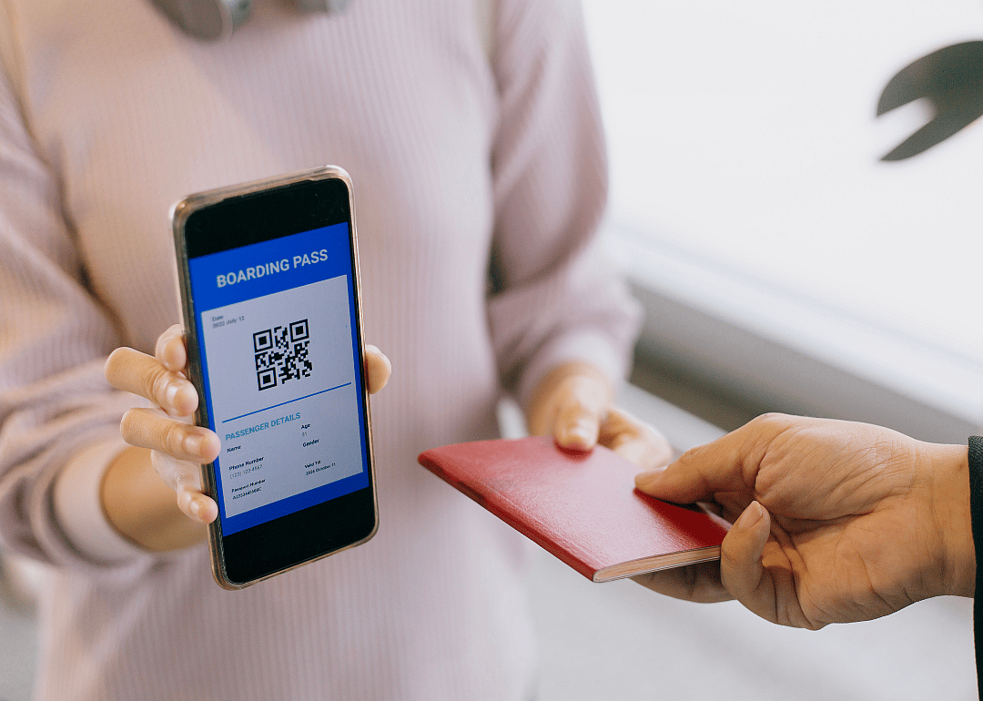 A person holding up a phone with a mobile boarding pass, handing someone a passport.