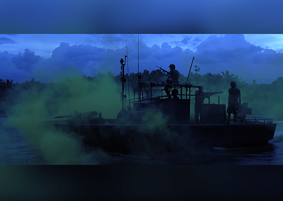 A silhouette of a boat with soldiers floats along a river in front of a deep blue and greeen sky