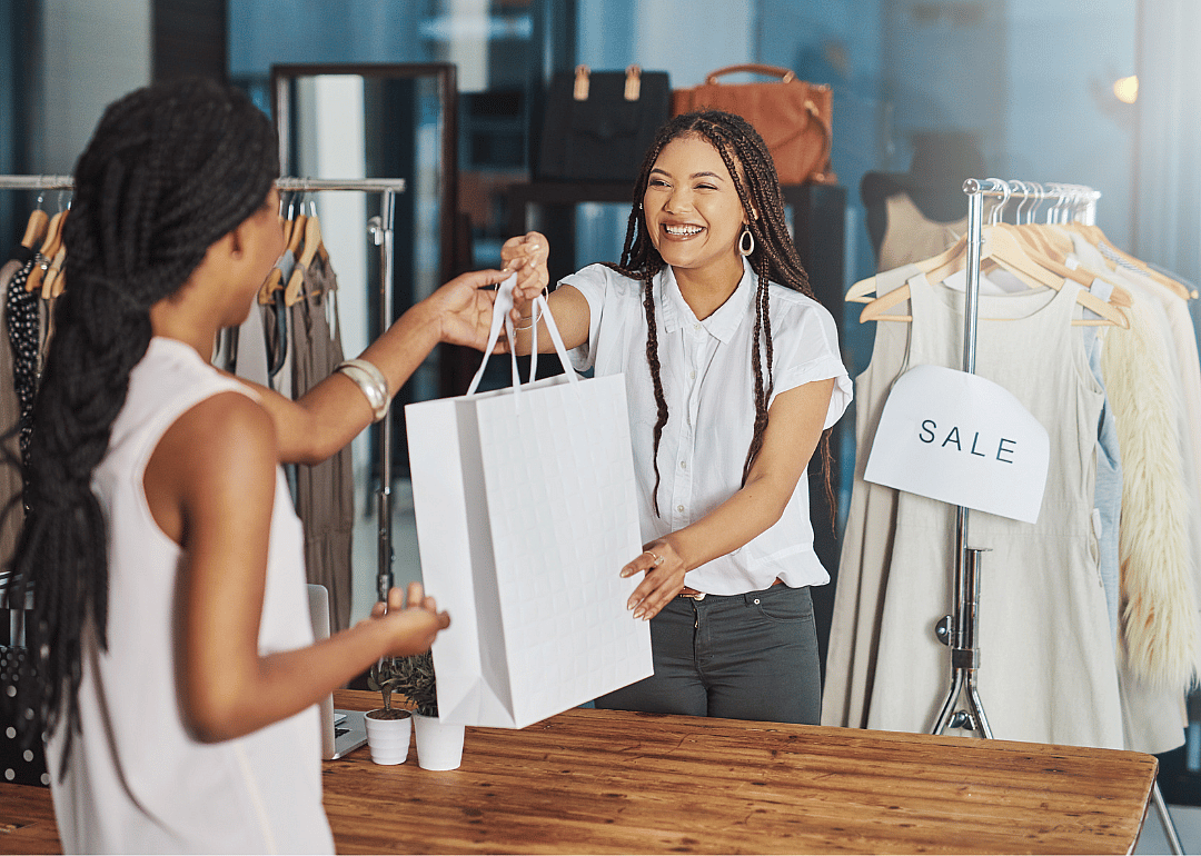 A shop assistant handing a shopping bag to a customer in a clothing boutique. 
