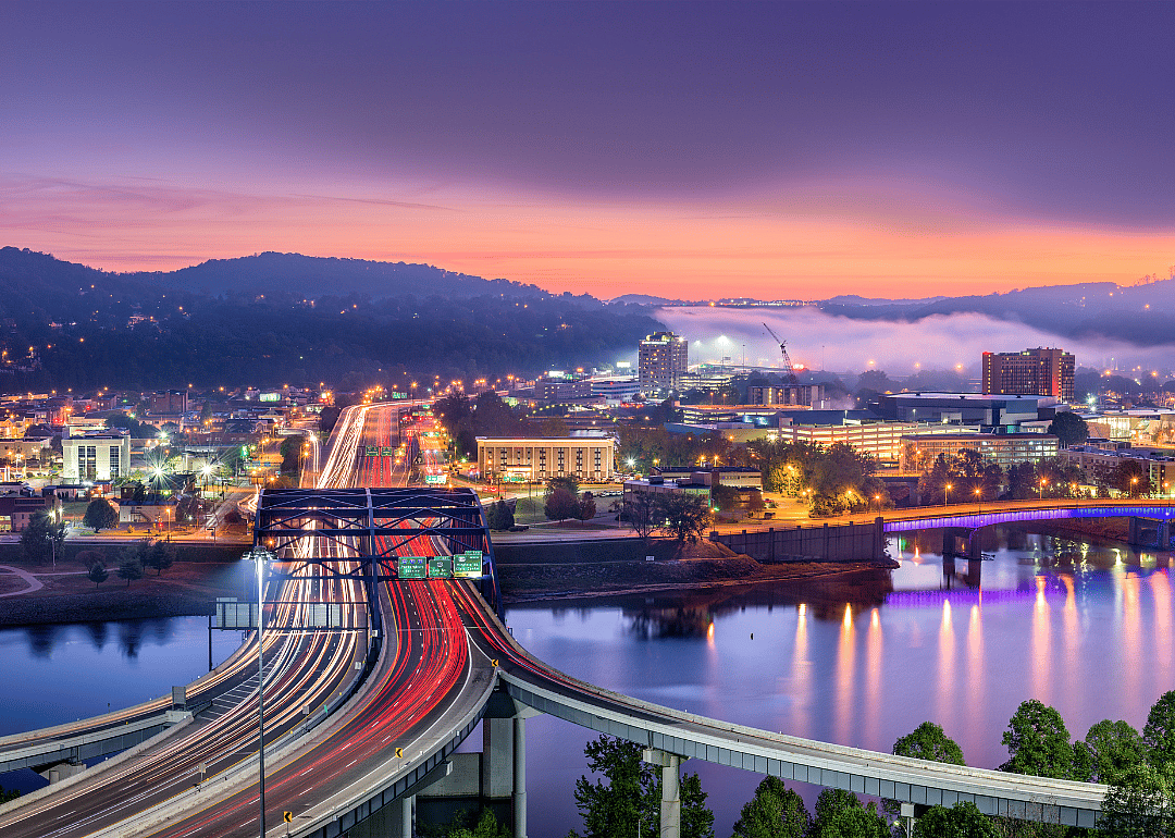 A city skyline with a bridge over a river at sunset.