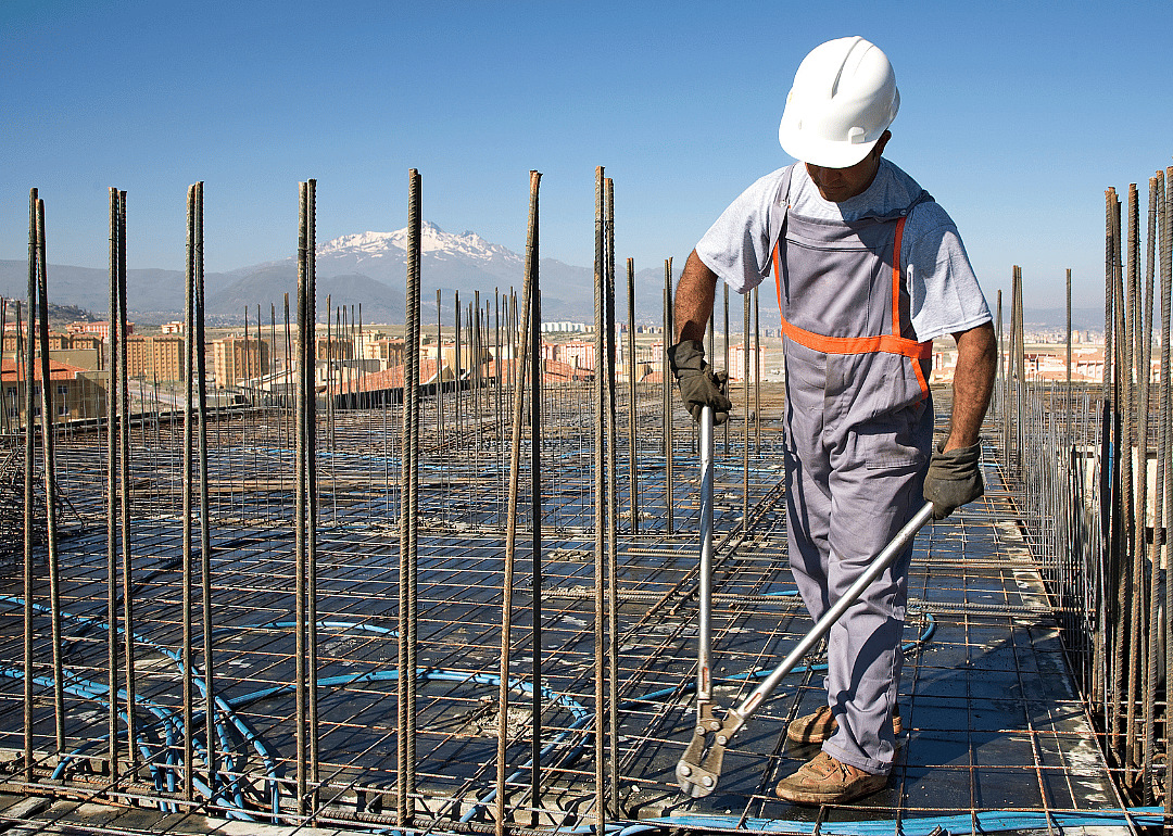 A construction worker holding a long pair of pliers outside.