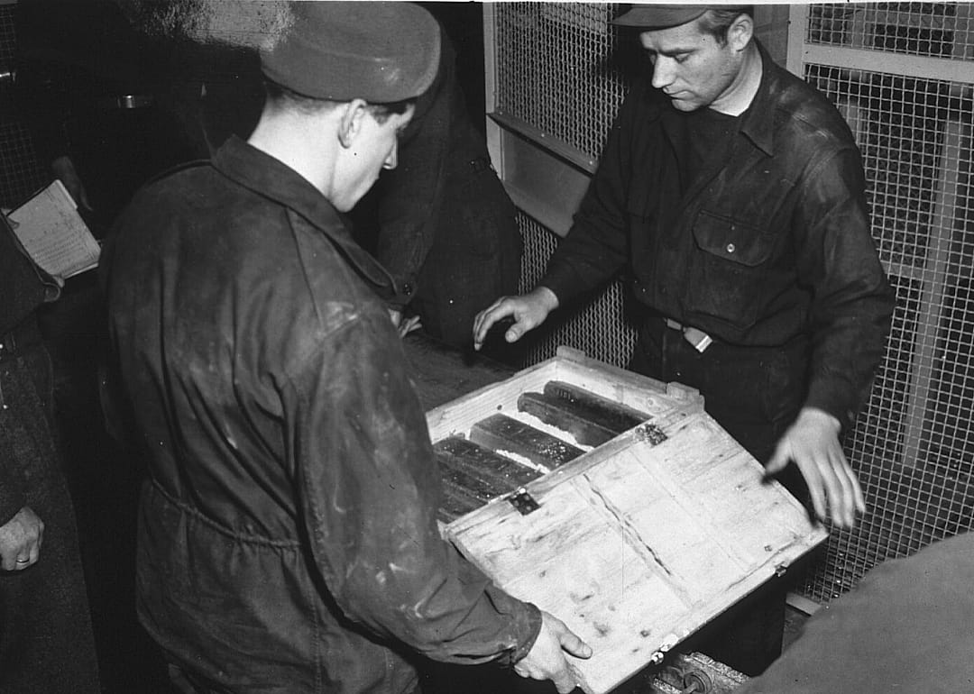 Two men open a box of gold bars. 