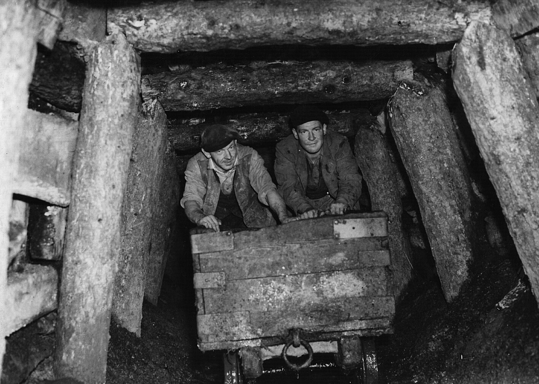 Two miners ride a cart inside a mine shaft.