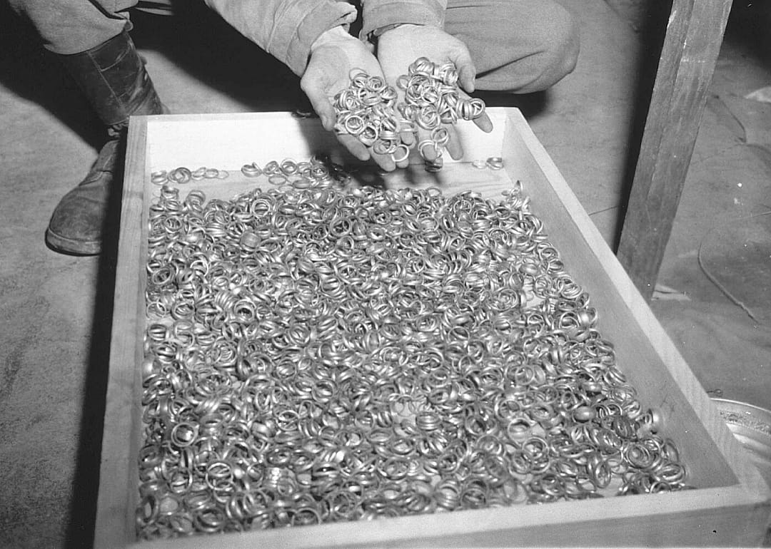 A man displays a handful of gold rings taken from a large bin.