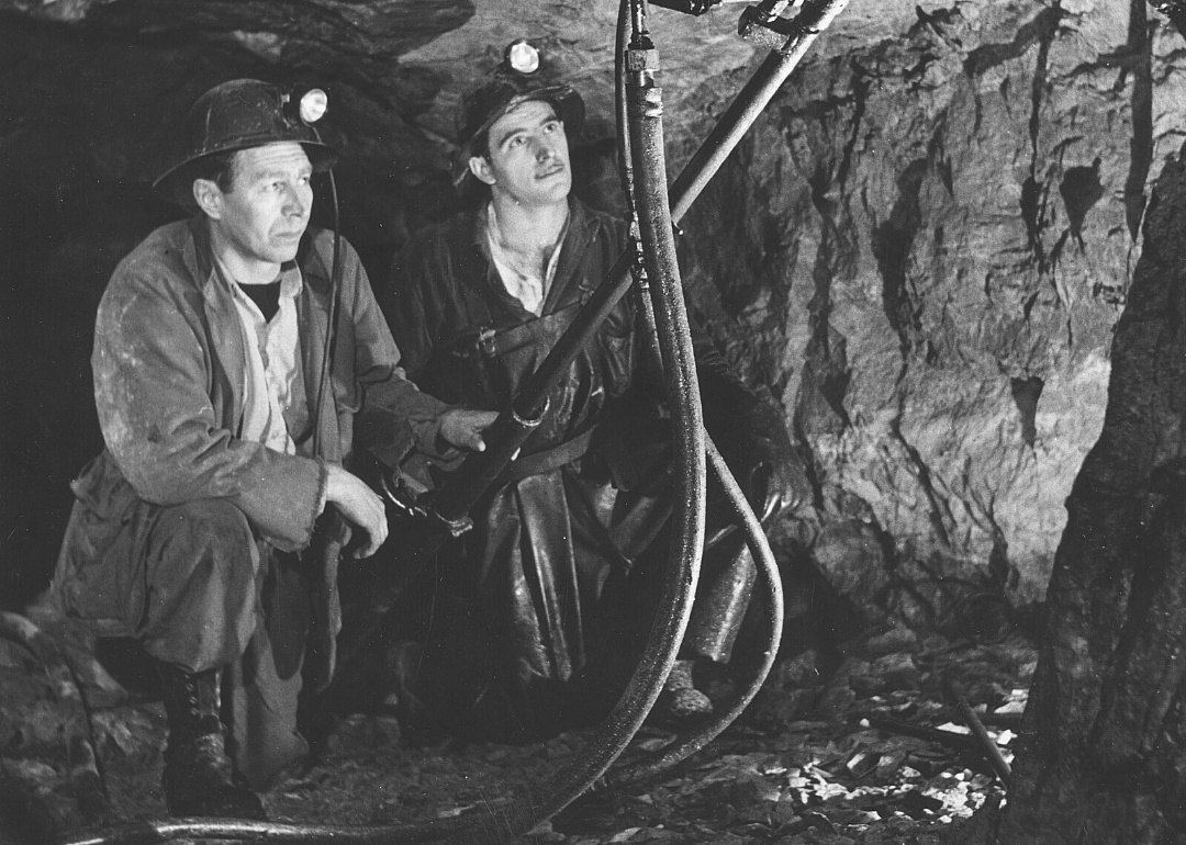 Two miners work with tools in a mine shaft.