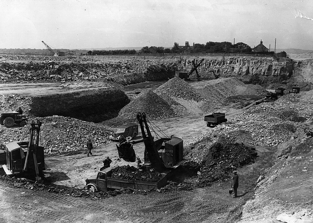 Cranes load material into trucks at a mining site.