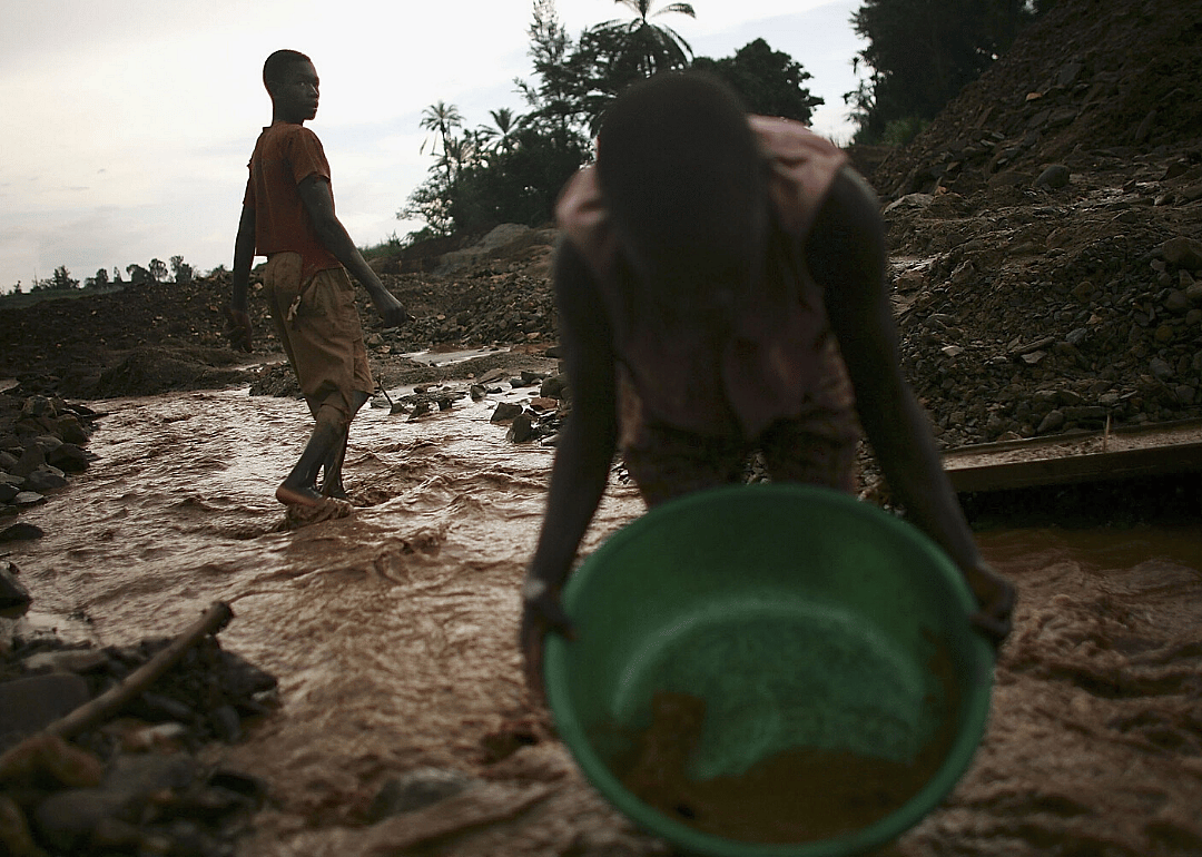 Two boys pan for gold in a small mining operation.