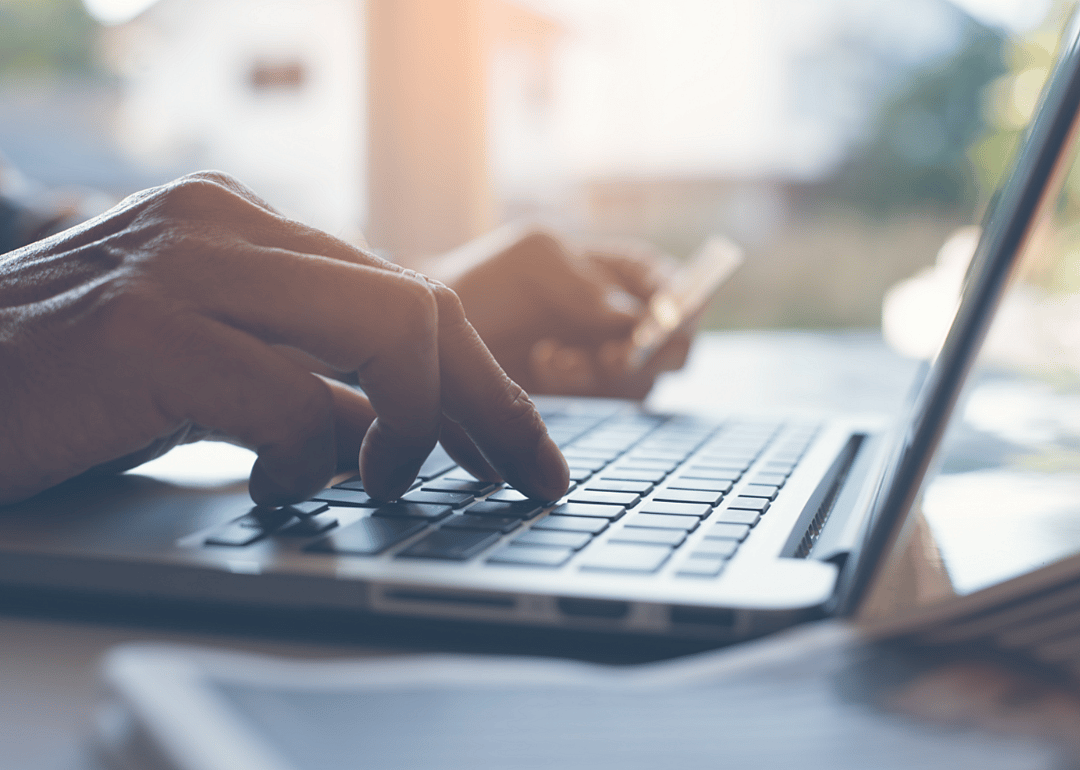 A man holding a credit card in one hand and types on a laptop with the other.