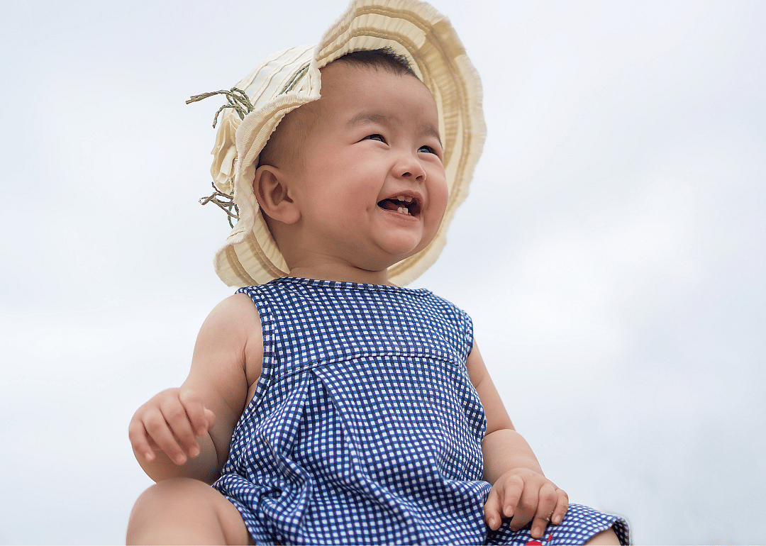 Asian baby girl smiling in summer dress and hat.