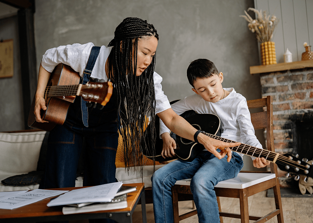 A female music teacher showing a student cords on a guitar.