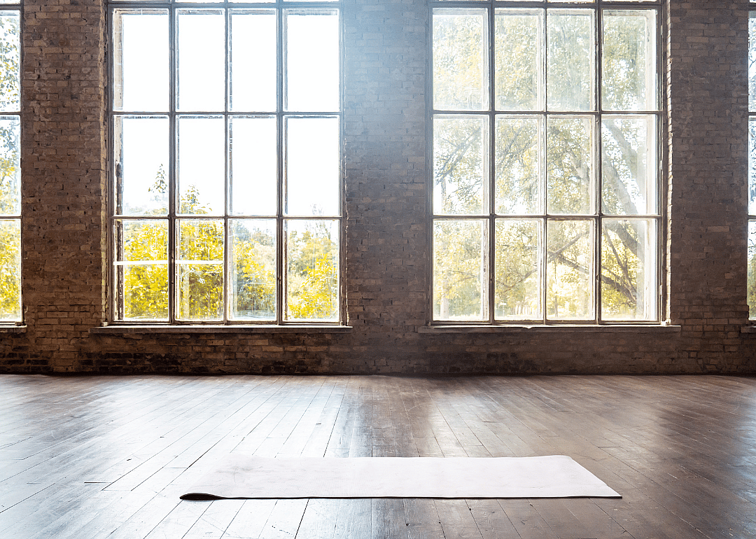 A yoga mat on a wooden floor in front of big windows.