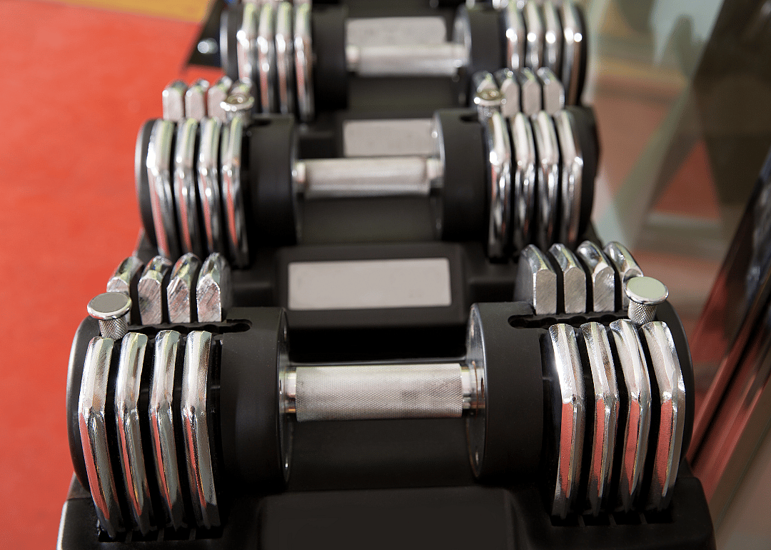 Adjustable dumbbells on a rack in front of a red floor.