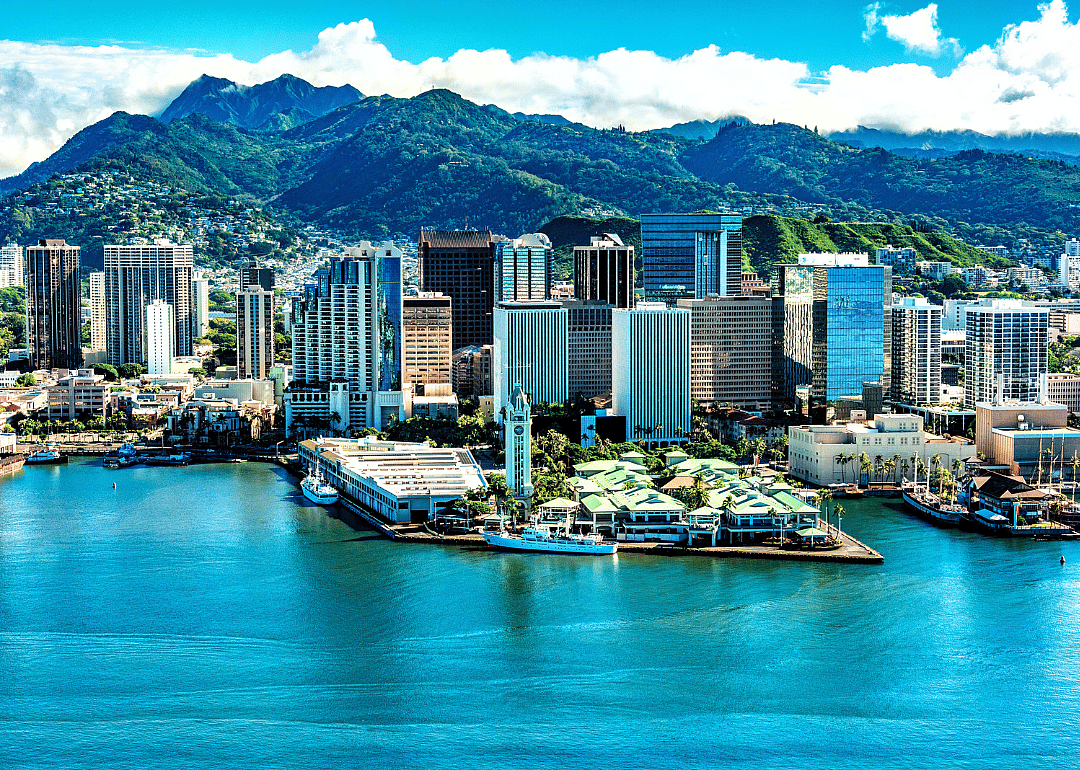 Tall buildings by the water with green mountains in the background.