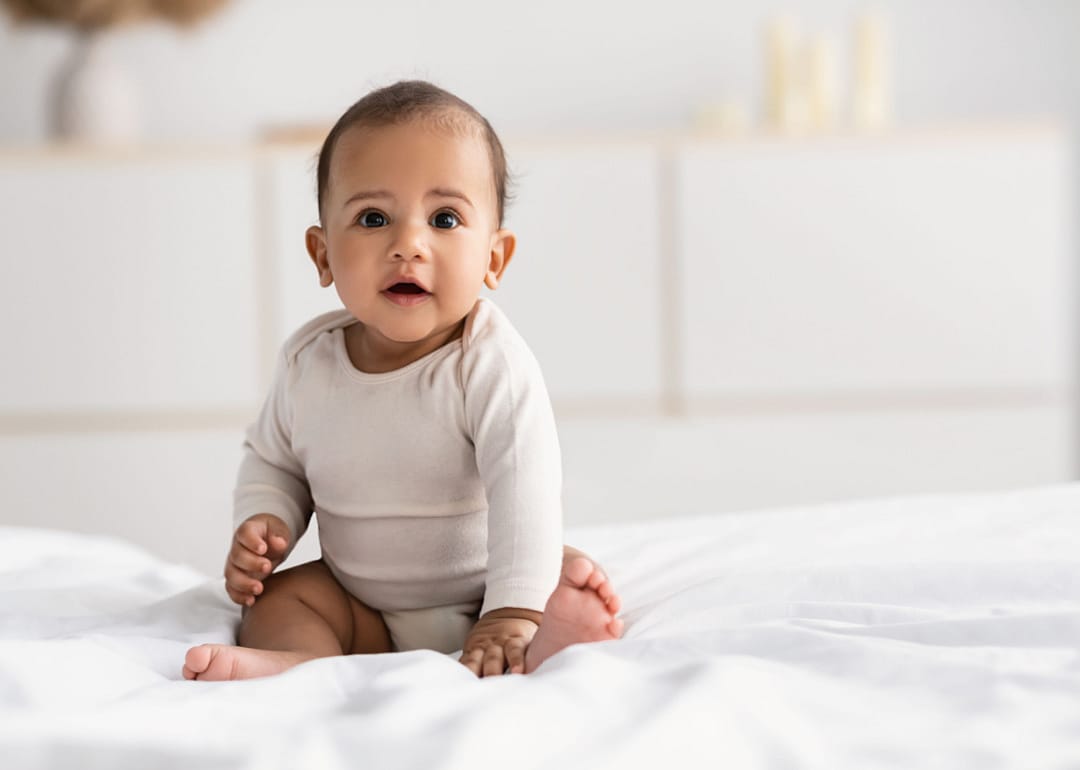 African American infant sitting on bed.
