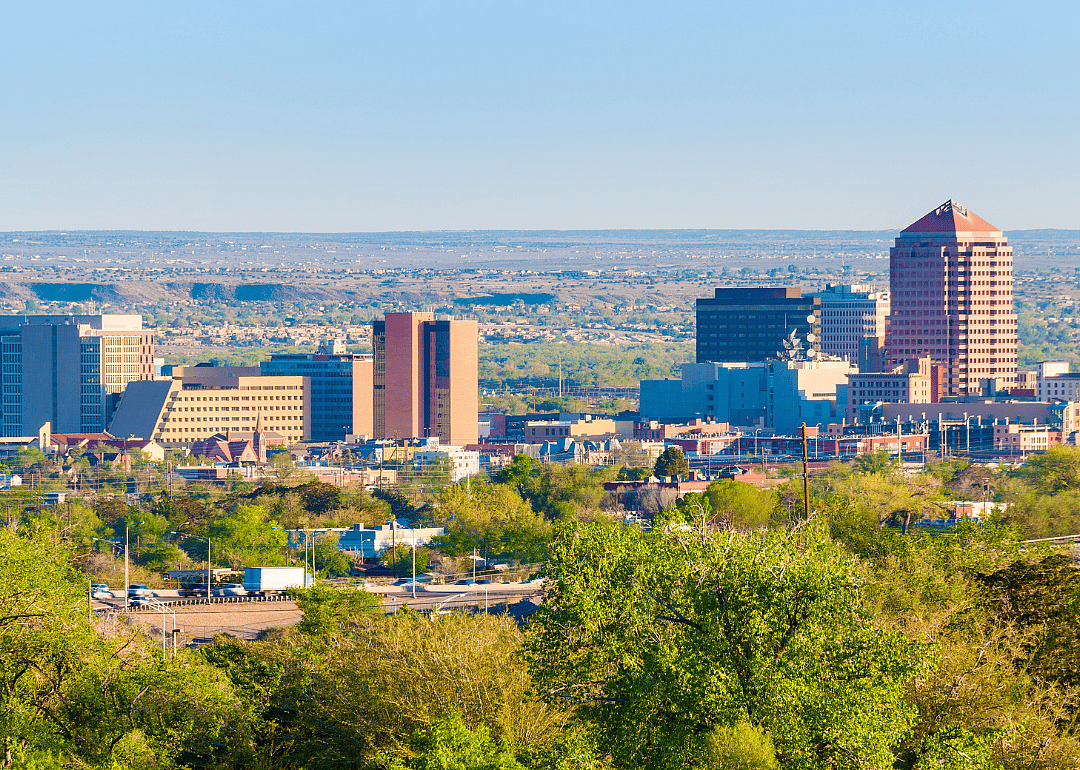 A city skyline with tall buildings and trees in the foreground.