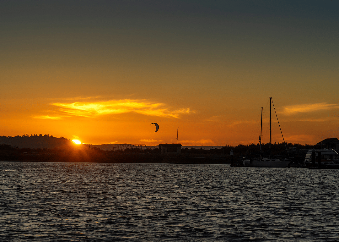 The sun setting over sailboats and a kite surfer on the water.