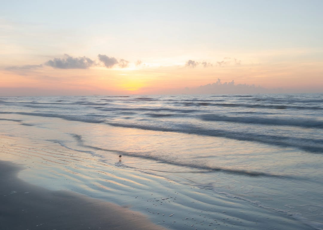 Waves lapping at the shore of a beach at sunrise.