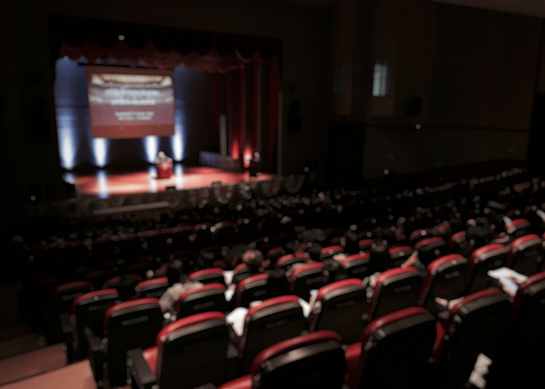 An auditorium filled with people as someone speaks on stage.