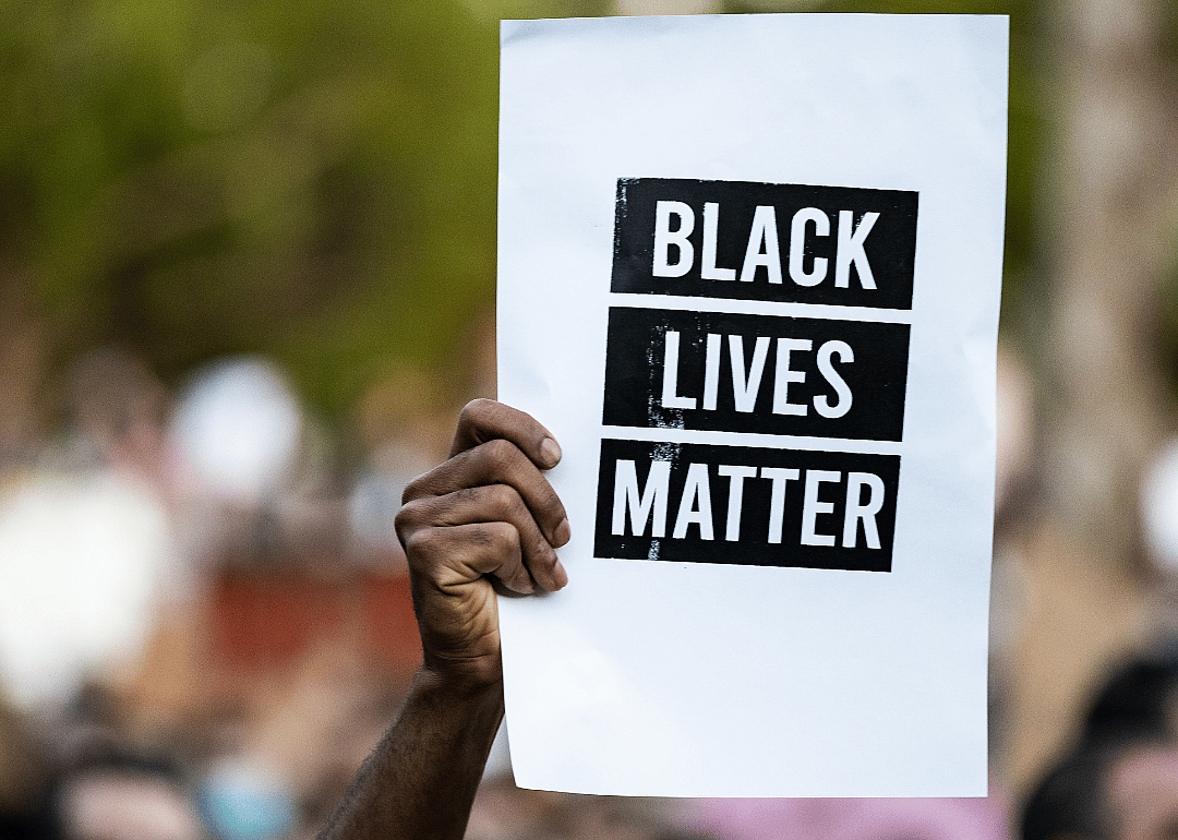 A hand holds up a sign reading Black Lives Matter in a crowd of people.