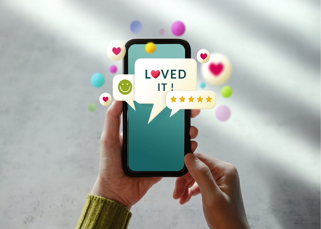 A photo illustration of a close up of hands holding a mobile phone with heart, smiling, and speech bubble emojis floating around it. 