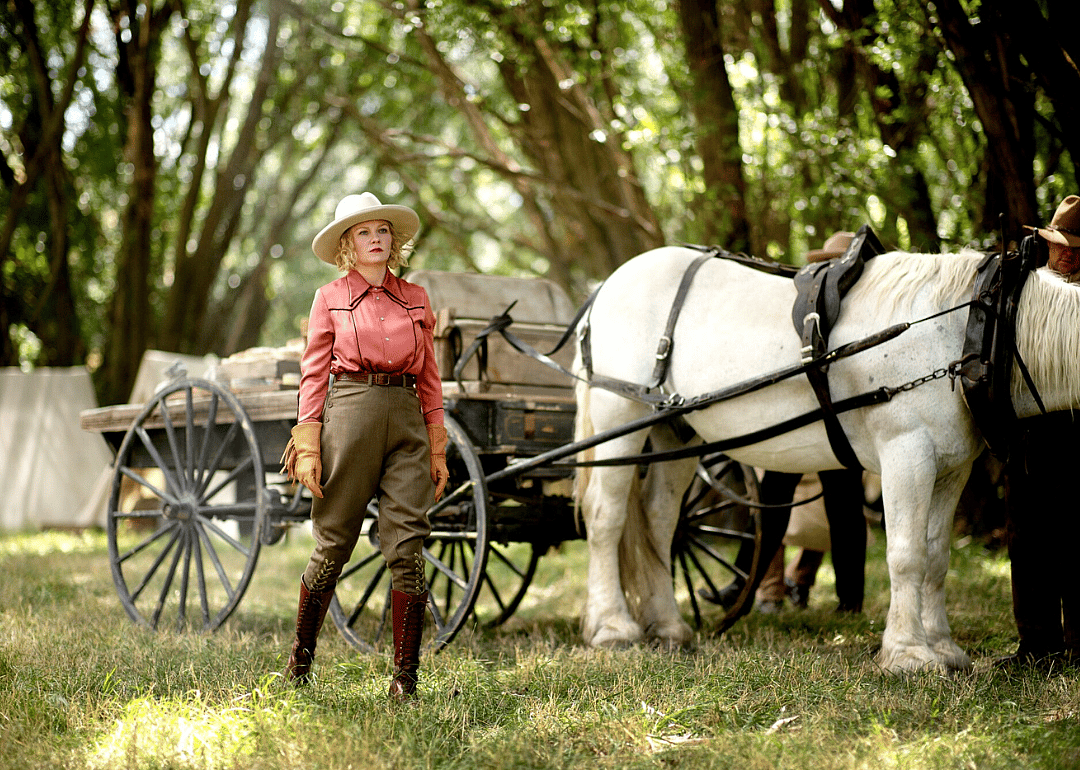 Kirsten Dunst in western clothing in front of a horse and wagon.