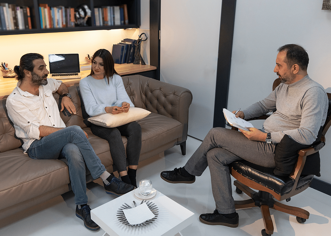 A psychiatrist talks to two people sitting next to each other on a couch.
