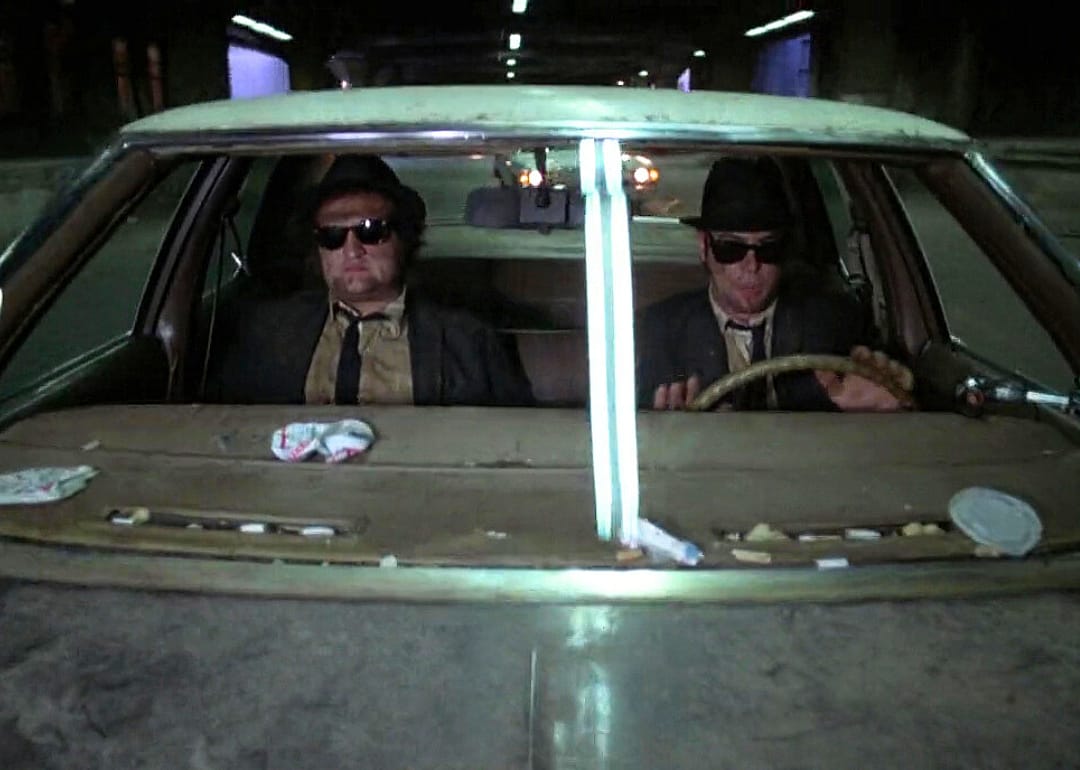 John Belushi and Dan Aykroyd covered in dirt in a messy car.