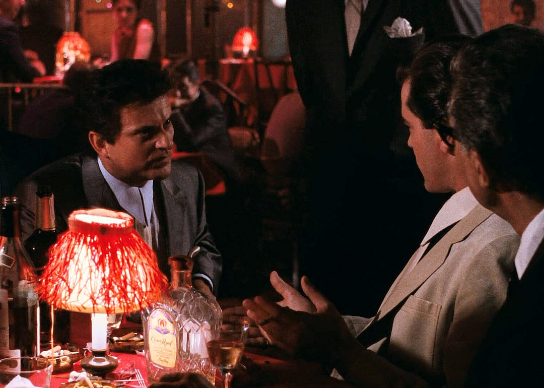 Joe Pesci talking to Ray Liotta at a table with a red lamp in a dark restaurant.