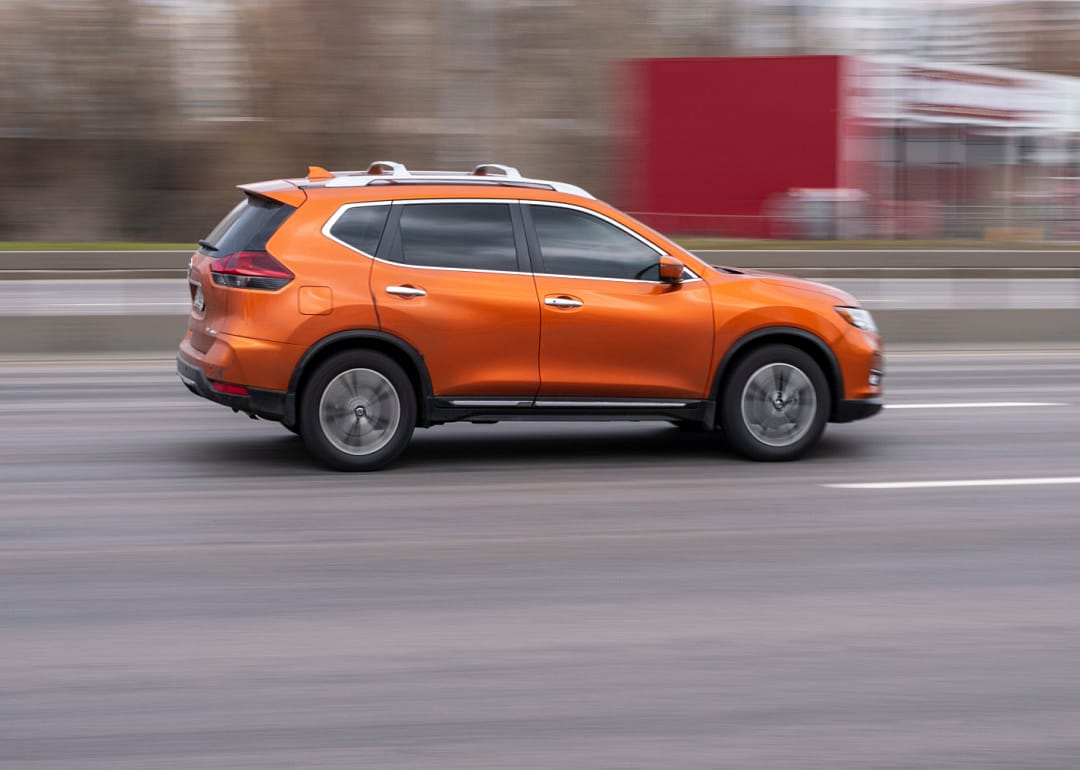 An orange Nissan Rogue speeding down the road.