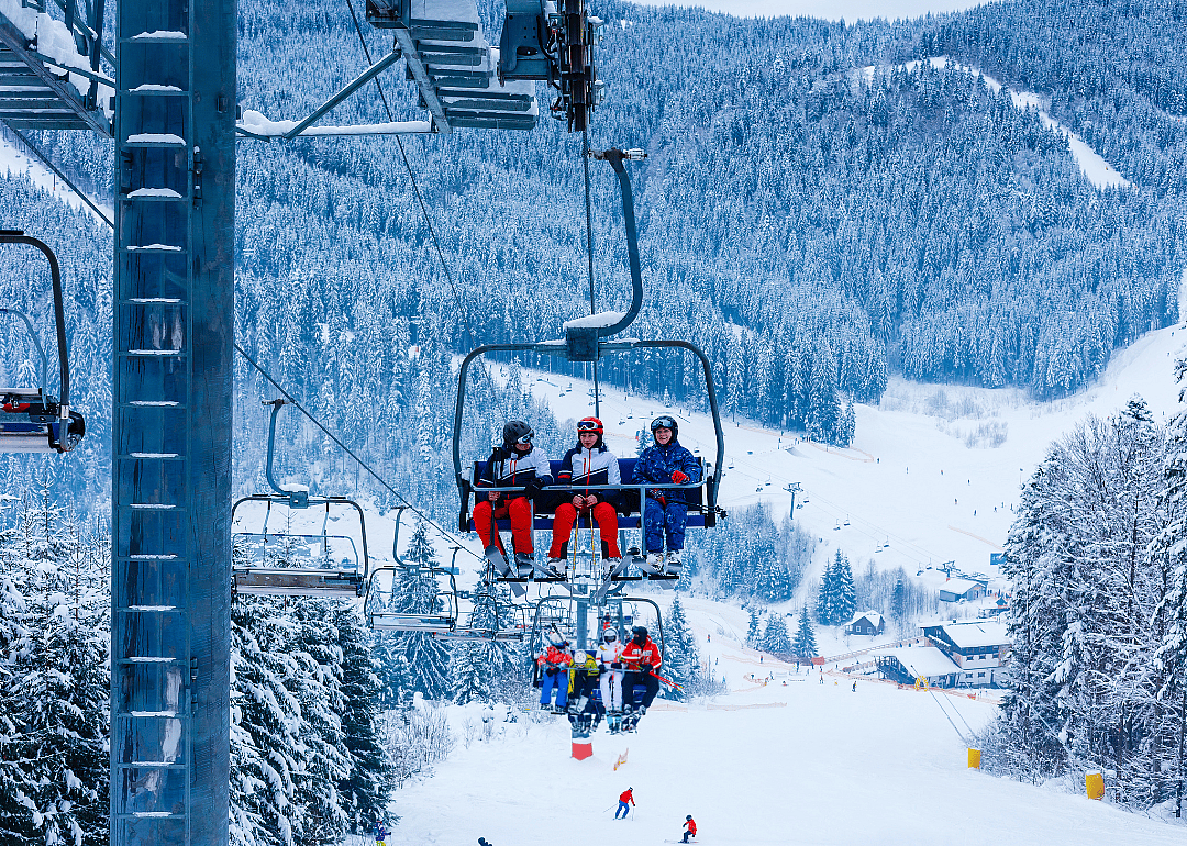 Ski lift with people going up the mountain and views of mountains covered in snow in the background.