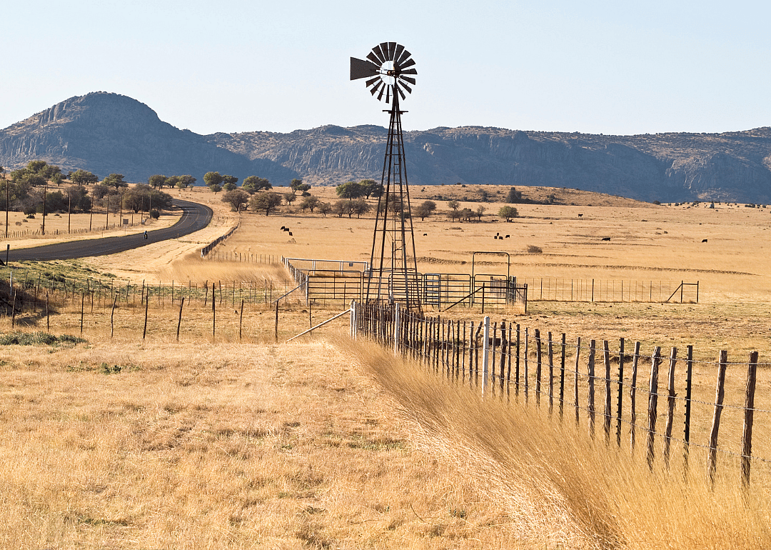 A windmill in the middle of a dry grass field. 
