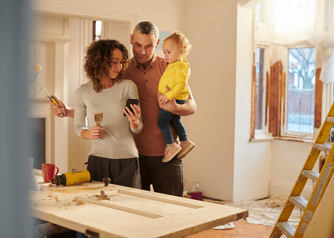 A family painting their house and looking at something on a cellphone.