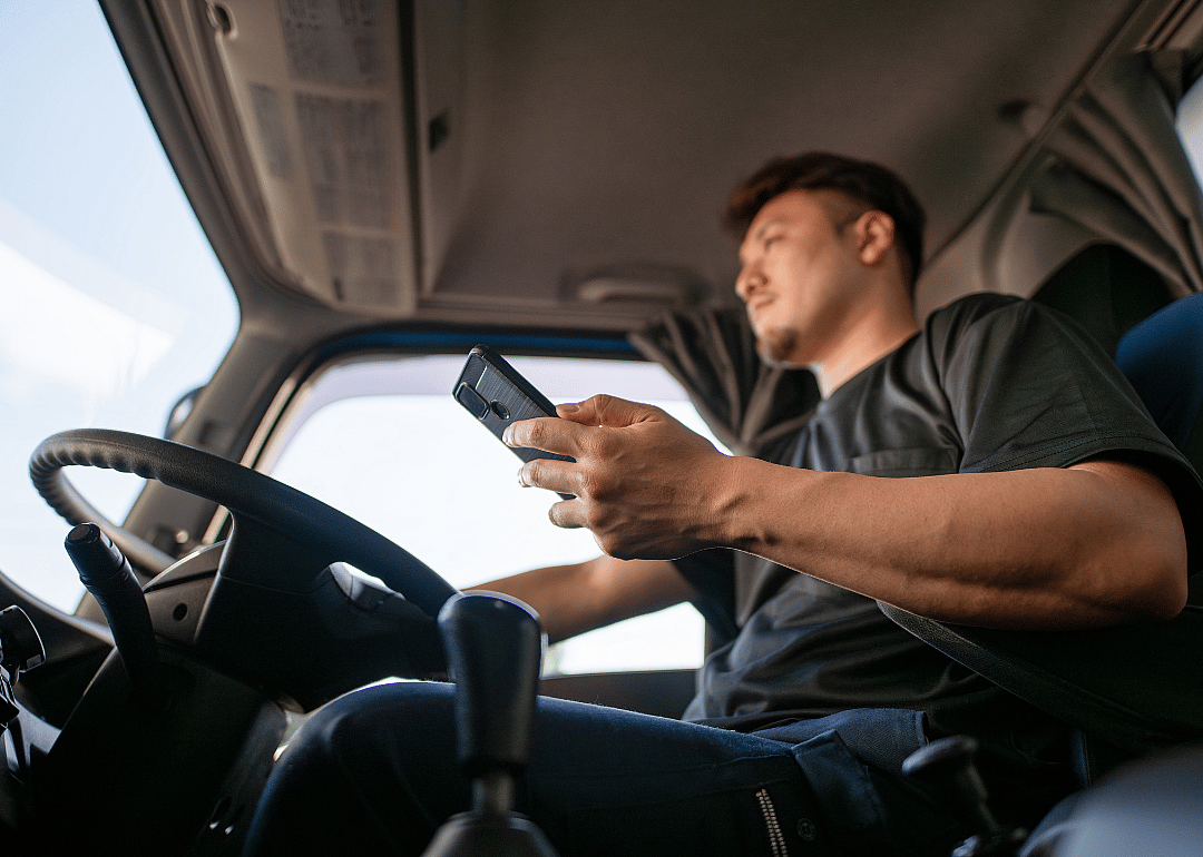 A trucker consults his smartphone inside his truck.