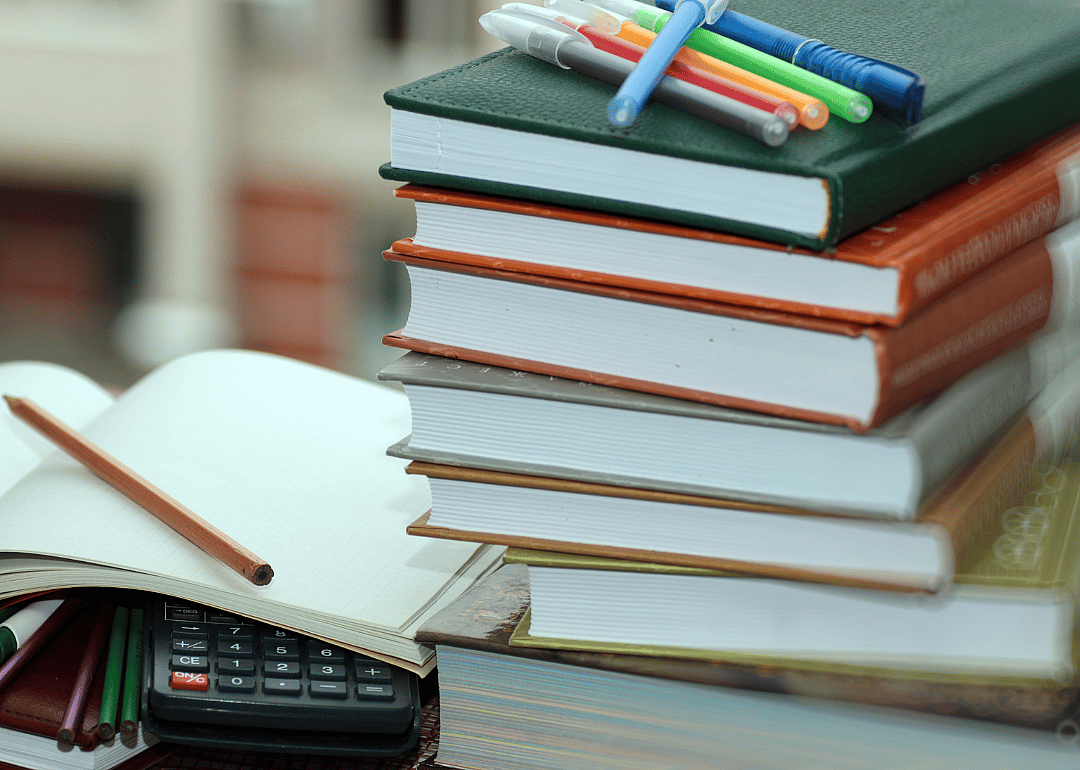 A stack of textbooks with pens on top of them next to an open notebook.